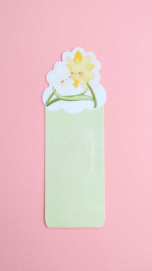 The Daffodil Hug Szn Spring Haze Green daffodil bookmark centered on a pink background. The shot captures a soft gloss sheen on the protective laminate, emphasizing the desaturated, pale green tones of this specific variant for color-obsessed desk-scaping.