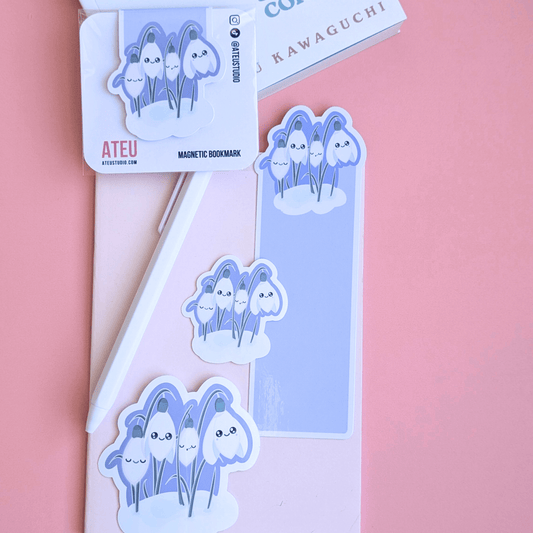 An airy reading nook scene featuring an Ateu Studio Sleepy Snowdrop 'Midnight Mist' Lavender Blue stationery set styled with Toshikazu Kawaguchi’s 'Before the Coffee Gets Cold.' The Snowdrop White characters with a cozy soft-glow effect are arranged on a pink pocket notebook, capturing a bright, breathable moment of aesthetic joy for book annotating.