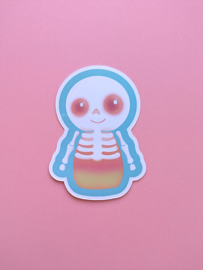 Skelicorn Luminous gloss vinyl sticker, a kawaii skeleton with a white skull and bones over a pastel candy corn body, turquoise outer detail and glowing Candy Coral pink eyes on a pink background.