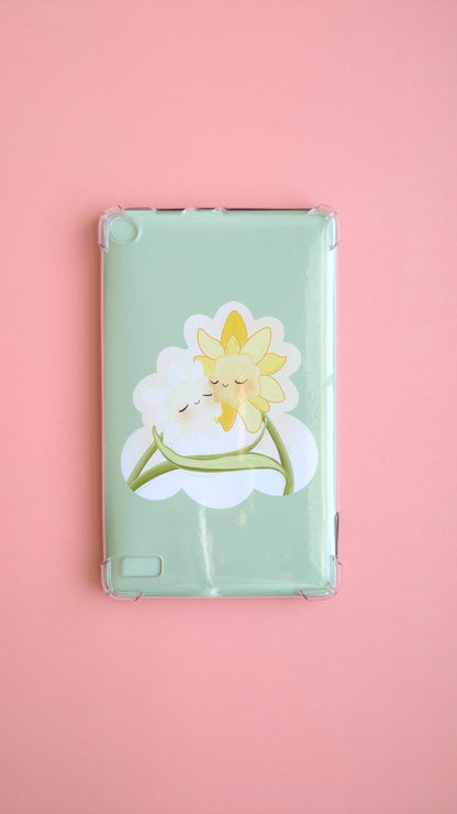 A naturally lit Kindle Paperwhite on a soft pink desk background featuring the 'Soft Glow' green kawaii Daffodil Hug Szn insert. The insert is shaped like an oversized die-cut sticker in warm daffodil yellow, reflecting light off its high-density gloss finish. A clean, adhesive-free tech-scape for intentional reading rituals.