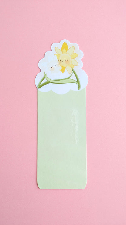 The Daffodil Hug Szn Spring Haze Green daffodil bookmark centered on a pink background. The shot captures a soft gloss sheen on the protective laminate, emphasizing the desaturated, pale green tones of this specific variant for color-obsessed desk-scaping.