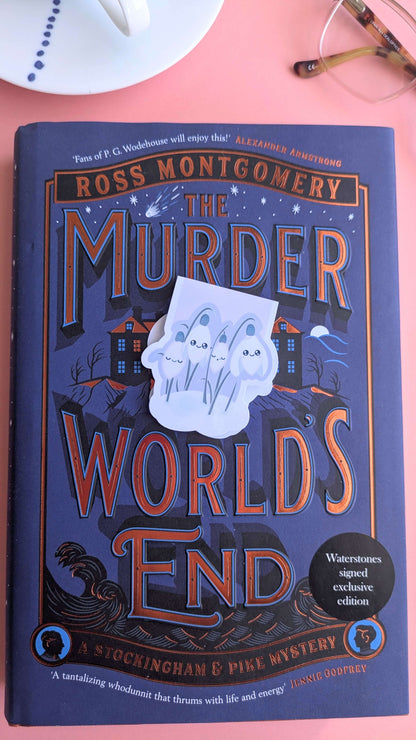 The Kawaii Sleepy Snowdrop 'Dawn' lavender blue magnetic bookmark angled to the right in the center of a signed exclusive edition book cover. Styled with a French porcelain cup and saucer showing hand-painted blue dot details, highlighting a mindful and aesthetic morning reading ritual.