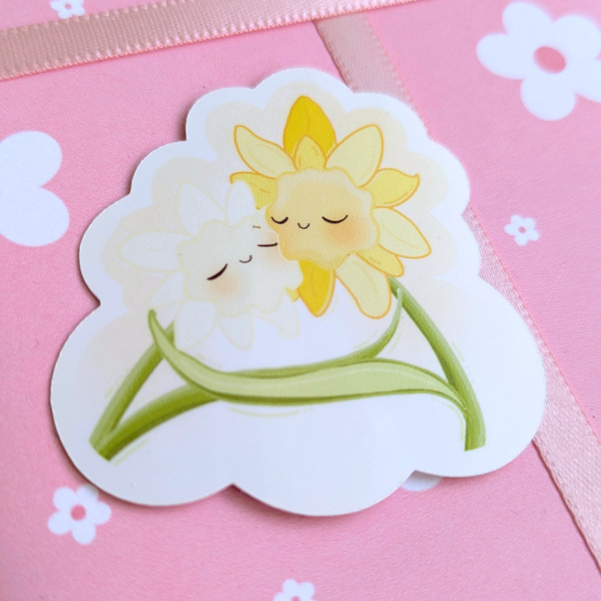 Ateu Studio Daffodil Hug SZN gloss sticker staged on daisy-patterned floral gift wrap. This high-detail aerial close-up features soft-face floral characters in a vibrant spring palette, perfect for aesthetic gift curation and intentional unboxing.
