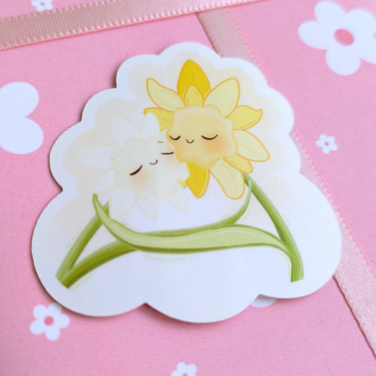 Ateu Studio Daffodil Hug SZN gloss sticker staged on daisy-patterned floral gift wrap. This high-detail aerial close-up features soft-face floral characters in a vibrant spring palette, perfect for aesthetic gift curation and intentional unboxing.