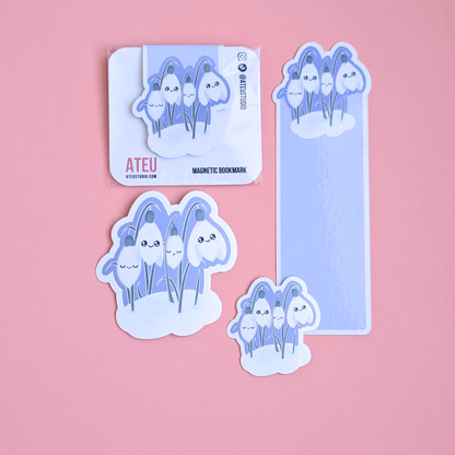 Ateu Studio Sleepy Snowdrop 'Midnight Mist' lavender blue Kawaii stationery gift set featuring Snowdrop White characters and a cozy soft-glow effect. The aerial view showcases the die-cut bookmark, magnetic bookmark, and two gloss vinyl stickers on a rose-pink background, highlighting the high-shine finish for Kindle decorating and gifting.