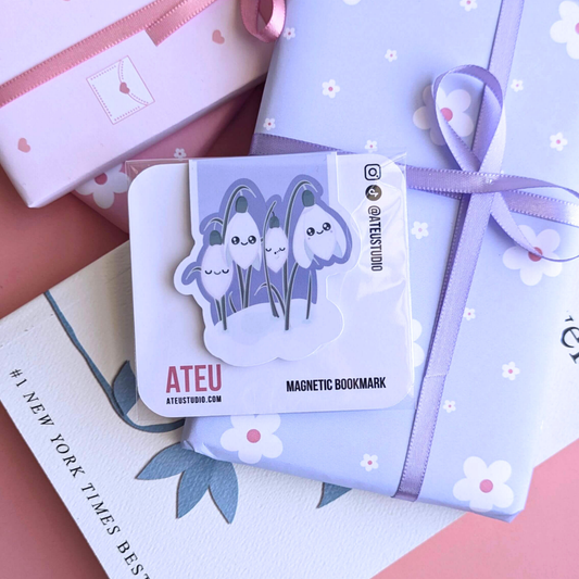 A close-up view of the Ateu Studio Kawaii Sleepy Snowdrop 'Midnight Mist' Lavender Blue magnetic bookmark on its branded backing card. The retail packaging shows the Kawaii character art clearly, with a soft light reflection. This shot highlights the premium presentation designed for aesthetic planning and book-safe decorating - an essential, book safe gift add-on for curated literary bundles.