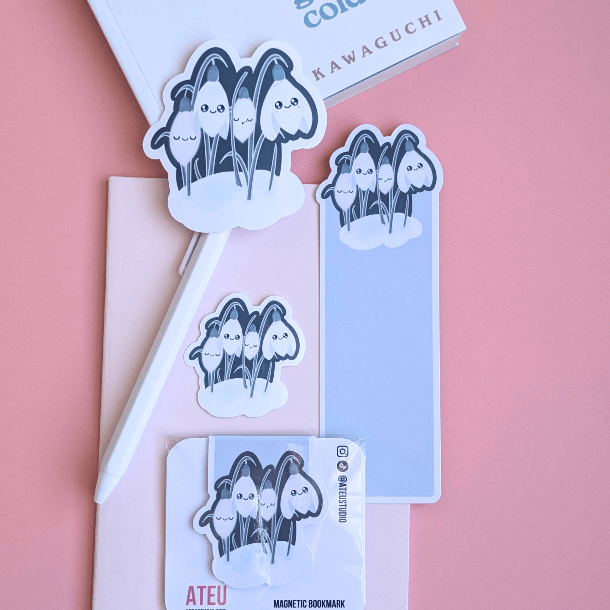 An airy reading nook scene featuring an Ateu Studio Sleepy Snowdrop atmospheric teal stationery set styled with Toshikazu Kawaguchi’s 'Before the Coffee Gets Cold.' The Snowdrop White characters with a cozy soft-glow effect are arranged on a pink pocket notebook, capturing a bright, breathable moment of aesthetic joy for book annotating. 