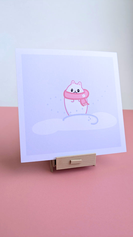 A 5x5 'Lil Beta Winter Storm Fern Mini Art Print' on a pink desk with a white wall behind it. The illustration shows Lil Beta against a lavender sky with star accents and a curved snowline, resting on a miniature wooden stand to highlight the smooth, reflection-free finish.