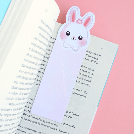 Close-up aerial view of the Marshmallow Blush Bunny Pink bookmark resting within the pages of Before the Coffee Gets Cold by Toshikazu Kawaguchi. The long ears extend beyond the page, and the vibrant pink background highlights the delicate kawaii cutie mark details on this Ateu Studio stationery piece.