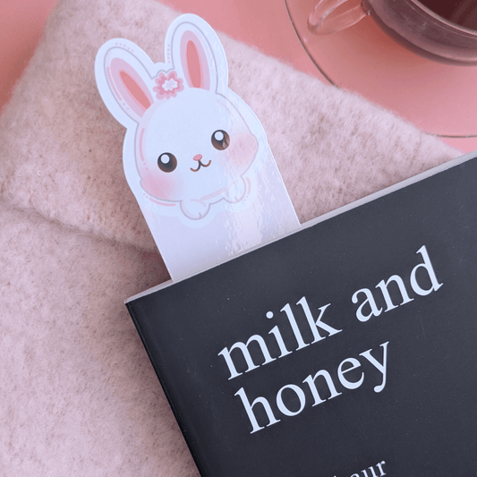 Close-up detail of the Marshmallow Blush Bunny Snowball White bookmark resting within the pages of Milk and Honey. Natural morning light catches the vibrant high-gloss sheen, highlighting the premium finish and intentional color palette of this Ateu Studio stationery piece.