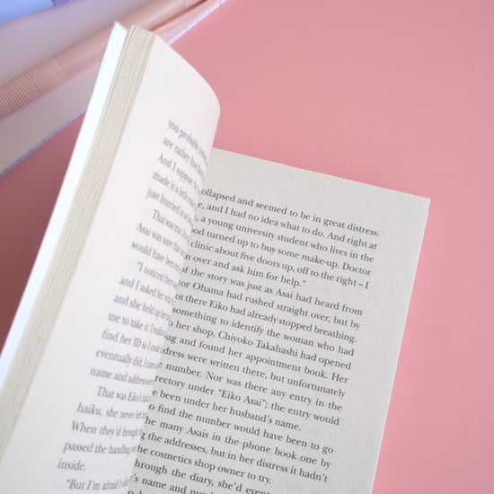 A point-of-view video showing a hand placing the Daffodil Hug Szn 'Sunny Shine' yellow magnetic bookmark onto a book page and gently 'booping' it closed with an index finger. The video highlights the satisfying magnetic snap and secure grip of the gloss-finish bookmark before the book is closed. The coordinated daisy gift wrap and pink stationery in the background reinforce the Ateu Studio aesthetic for mindful reading rituals.