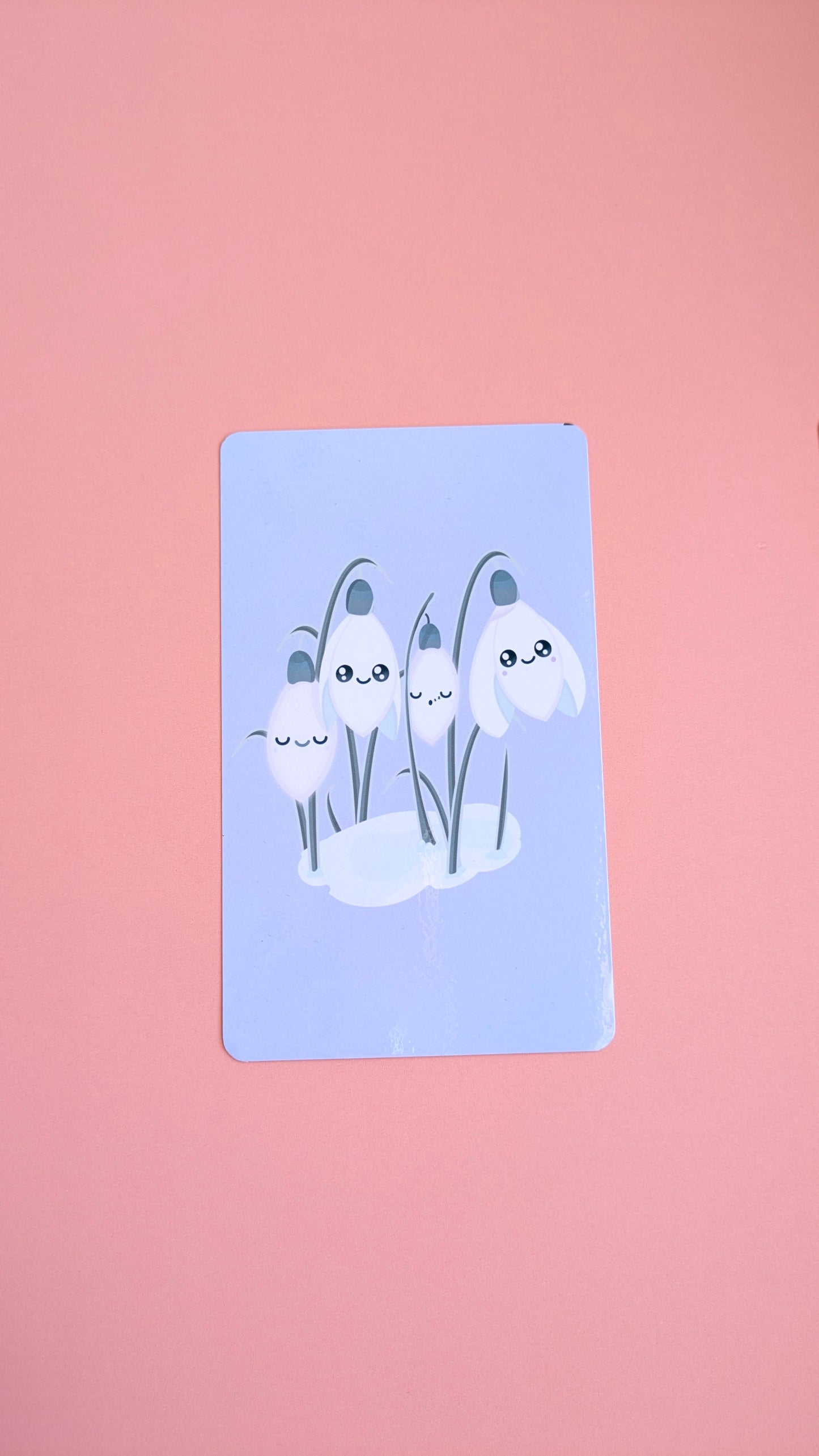 An aerial view of the 'Sleepy Snowdrops Dawn Lavender Blue Kindle Paperwhite Insert' resting on a soft pink background. The high-res photo media features the original kawaii characters in a morning sky palette with a clear gloss finish.