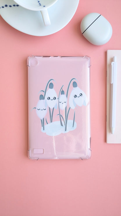 A centered Kindle with the 'Sleepy Snowdrops Icy Venusian Pink Kindle Paperwhite Insert' inside a clear case. This breathable arrangement features a dominating fine porcelain cup and saucer, Pixel Buds, and a sliver of a pink notepad and white pen for a clean, intentional reading ritual.
