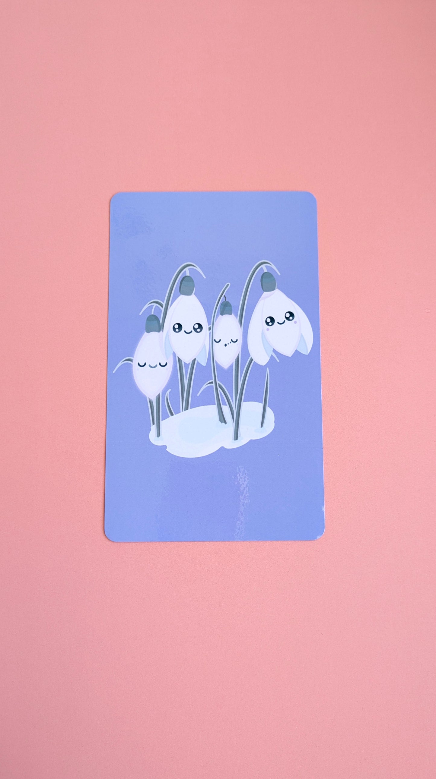 An aerial view of the 'Midnight Mist' lavender-blue Kindle Paperwhite insert resting on a soft pink background. The high-res photo media reveals original kawaii Sleepy Snowdrops characters against a winter sky, highlighting the high-gloss finish and monochrome aesthetic for Kindle decorating.
