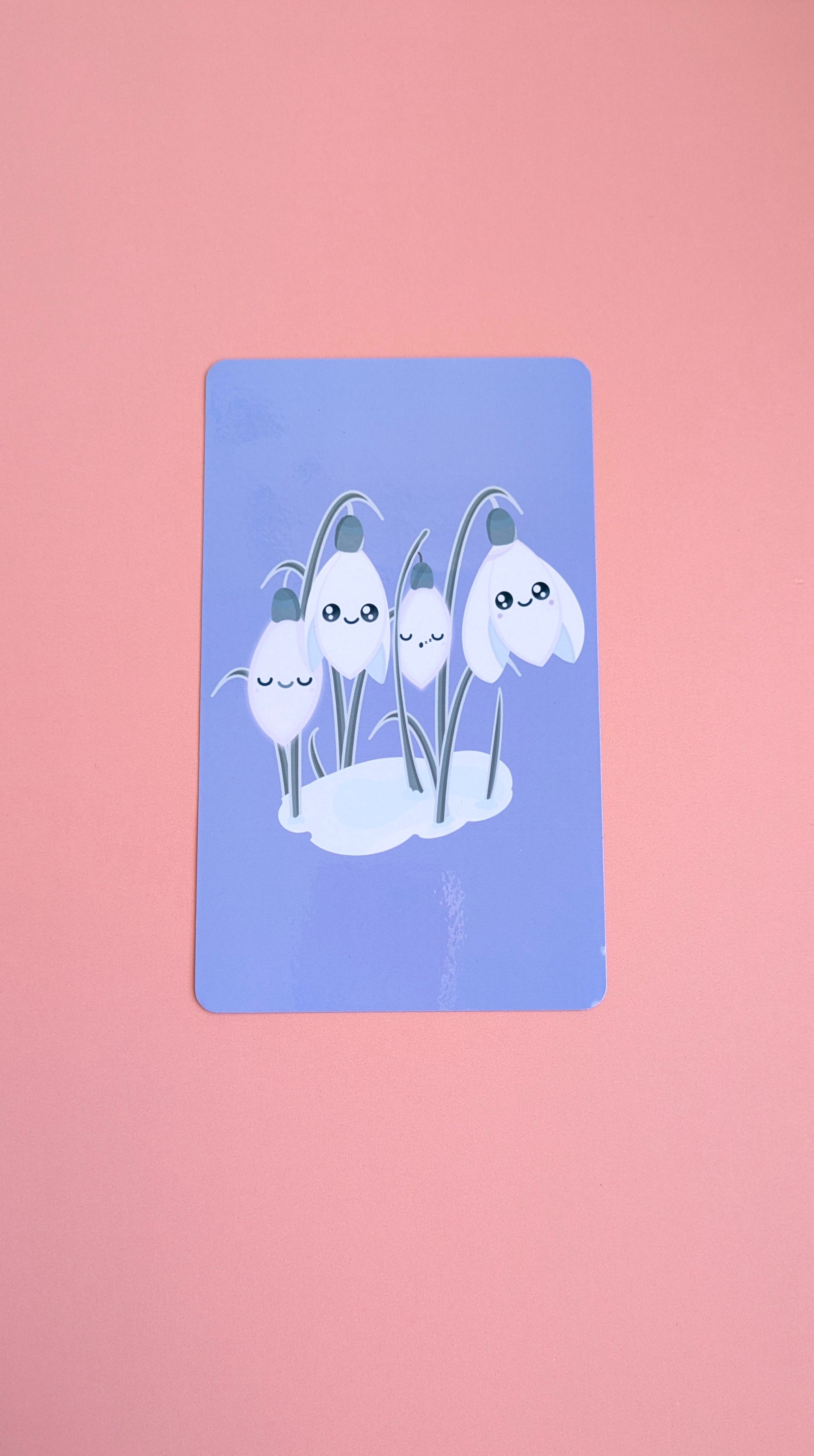 An aerial view of the 'Midnight Mist' lavender-blue Kindle Paperwhite insert resting on a soft pink background. The high-res photo media reveals original kawaii Sleepy Snowdrops characters against a winter sky, highlighting the high-gloss finish and monochrome aesthetic for Kindle decorating.