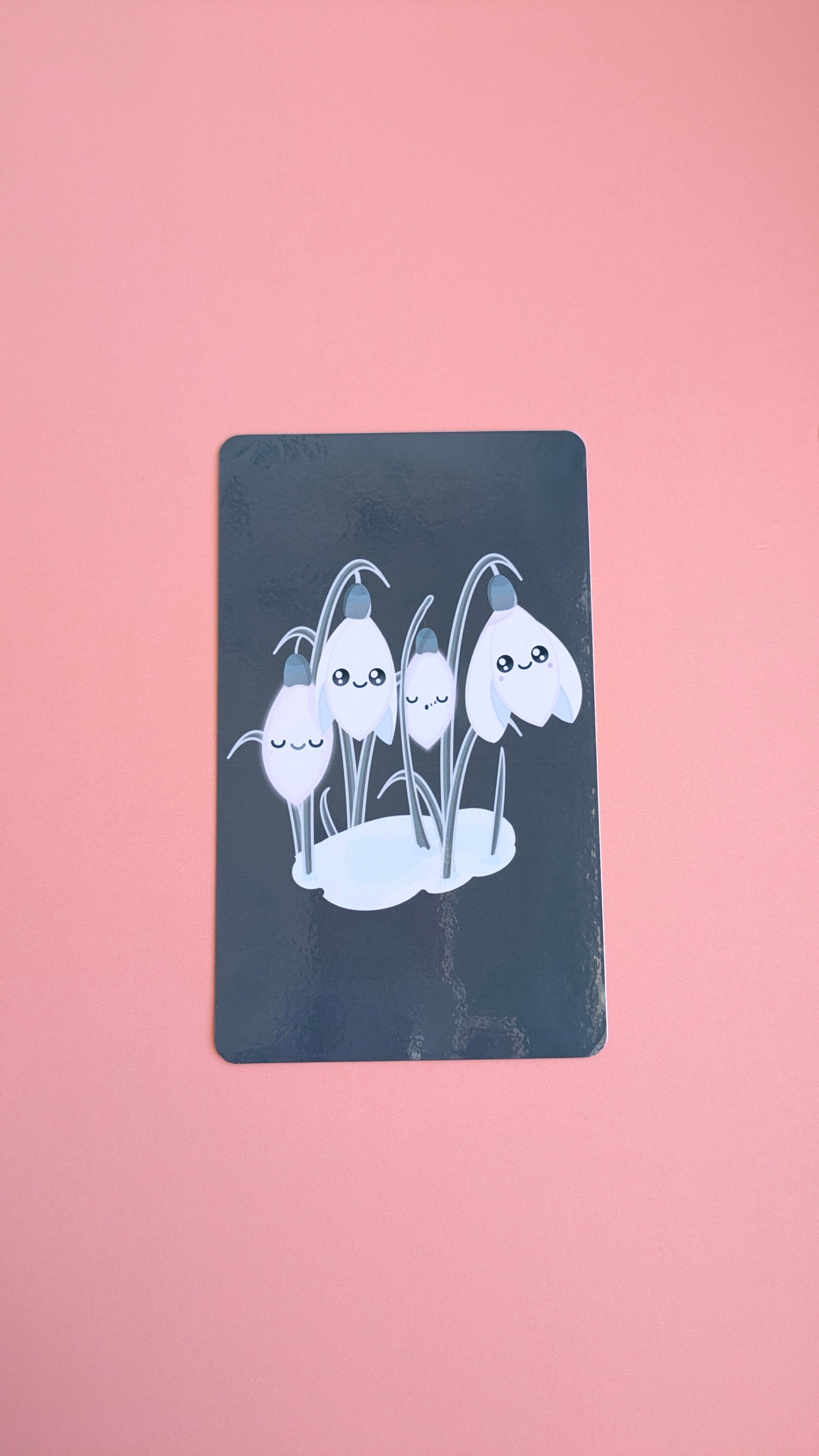An aerial, naturally lit view of the 'Sleepy Snowdrops Winter’s Edge Teal Kindle Paperwhite Insert' on a pink background. The high-res photo media features the original kawaii characters against a deep teal winter sky with a high-gloss finish.